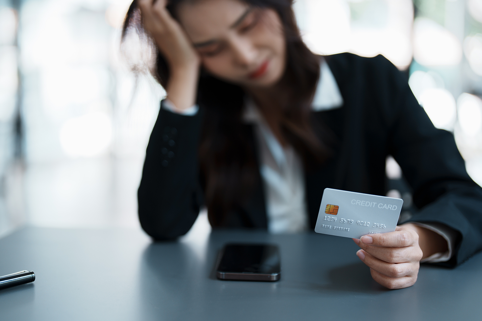 Portrait of young Asian woman holding credit card with smart phone mobile and showing worried expression on credit card debt.