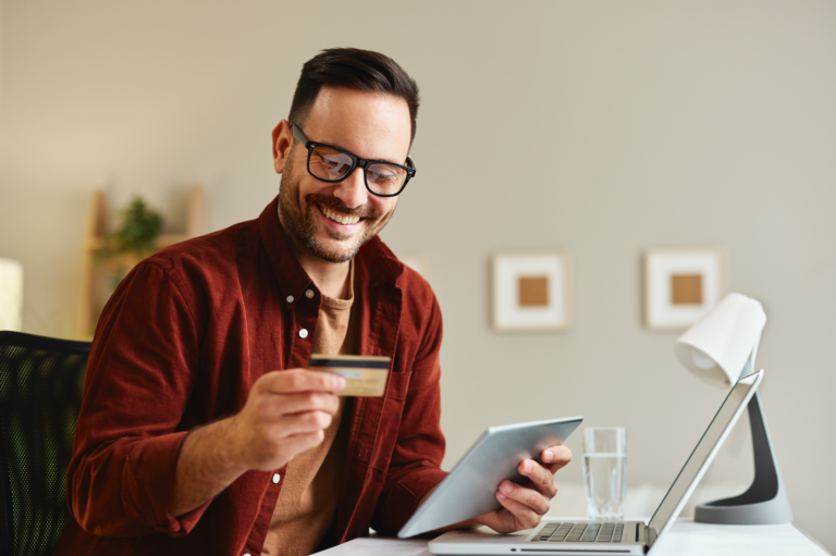 Young man holding credit card and tablet at home at table learning how to use credit cards responsibly