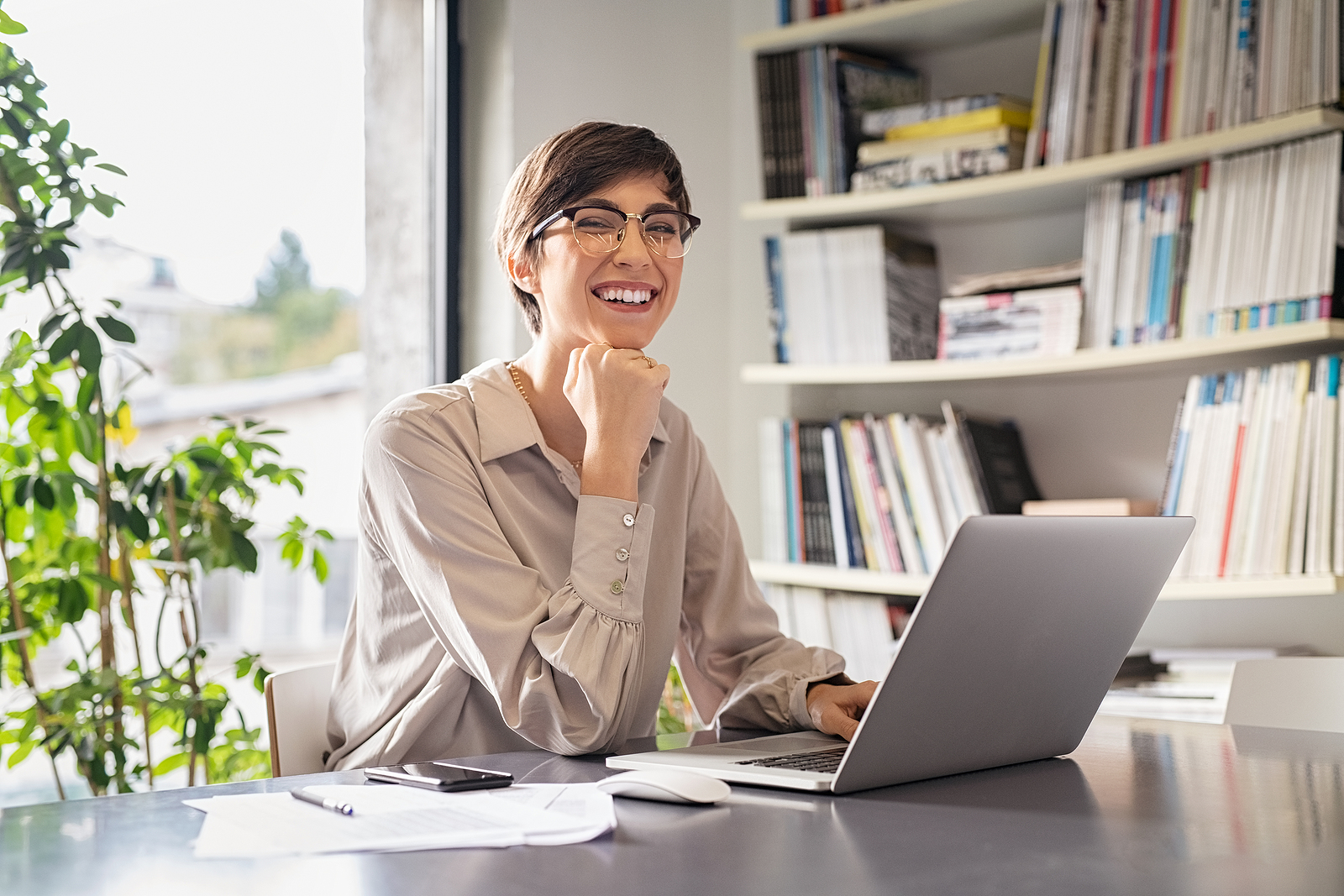 Successful young business woman sitting in creative office and looking at camera. Portrait of happy entrepreneur working on computer. Smiling businesswoman using laptop to start rebuilding credit after bankruptcy while working from home.