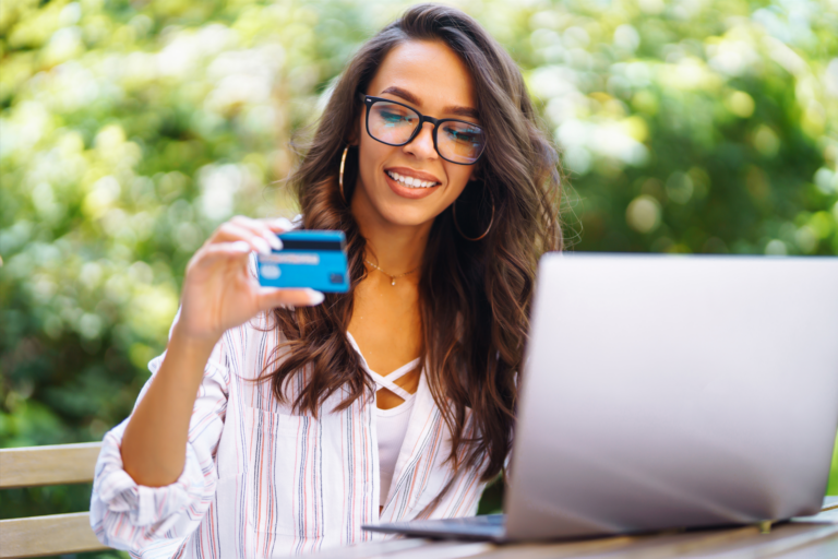 Young woman sitting at cafe with laptop using credit card after deciding between credit repair vs. credit building