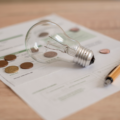 how to add utilities to your credit report Electricity bill with light bulb, several coins and pen on the desk. Concept of electricity prices