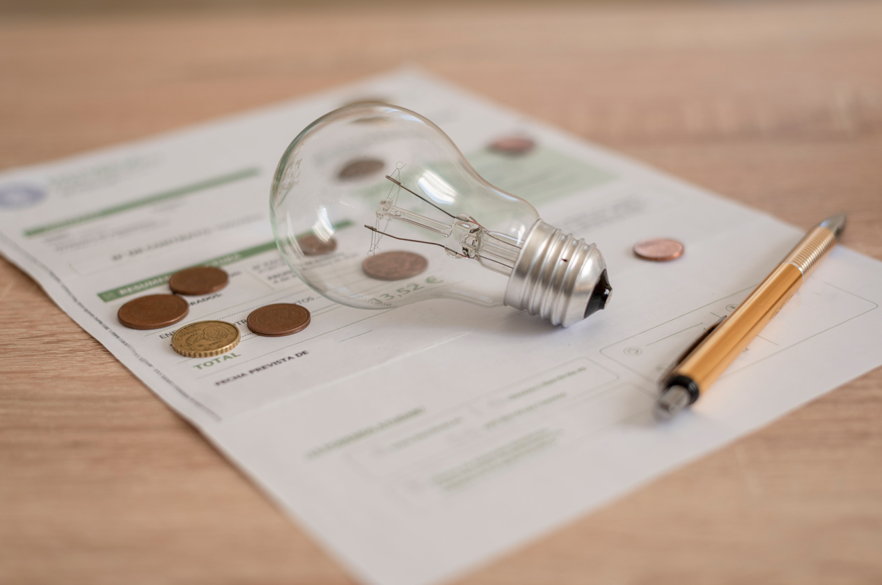 how to add utilities to your credit report Electricity bill with light bulb, several coins and pen on the desk. Concept of electricity prices