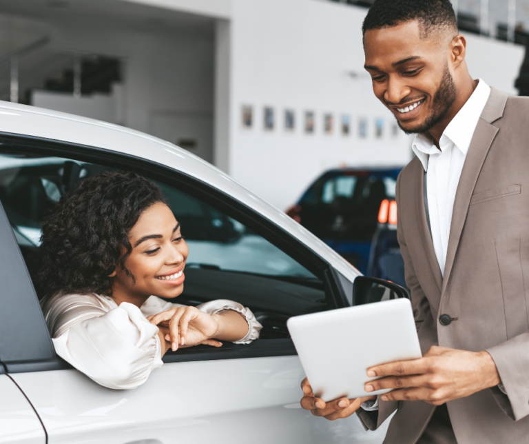 Car dealership salesperson showing financing options to a smiling customer representing preparing your credit for a car loan